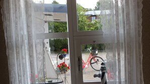 Une fenêtre avec un cadre blanc et des rideaux en dentelle, un vélo et une maquette de phare sur le rebord de la fenêtre.