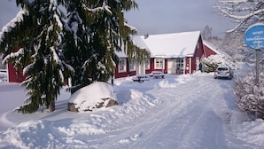 Une route de campagne enneigée menant à un bâtiment rouge avec une porte et des fenêtres blanches.
