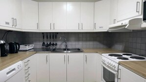 Una cocina moderna con armarios blancos, lavavajillas empotrado, estufa y cafetera.