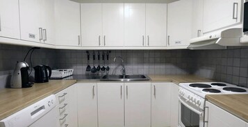 Uma cozinha moderna com armários brancos, lava-louças embutida, fogão e cafeteira.
