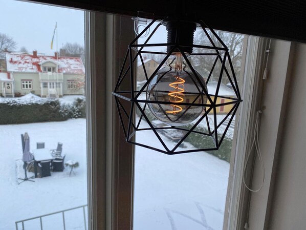A hanging light fixture with a visible spiral filament bulb, a window, and a snowy outdoor scene. - Vara Pensionat (Vara)
