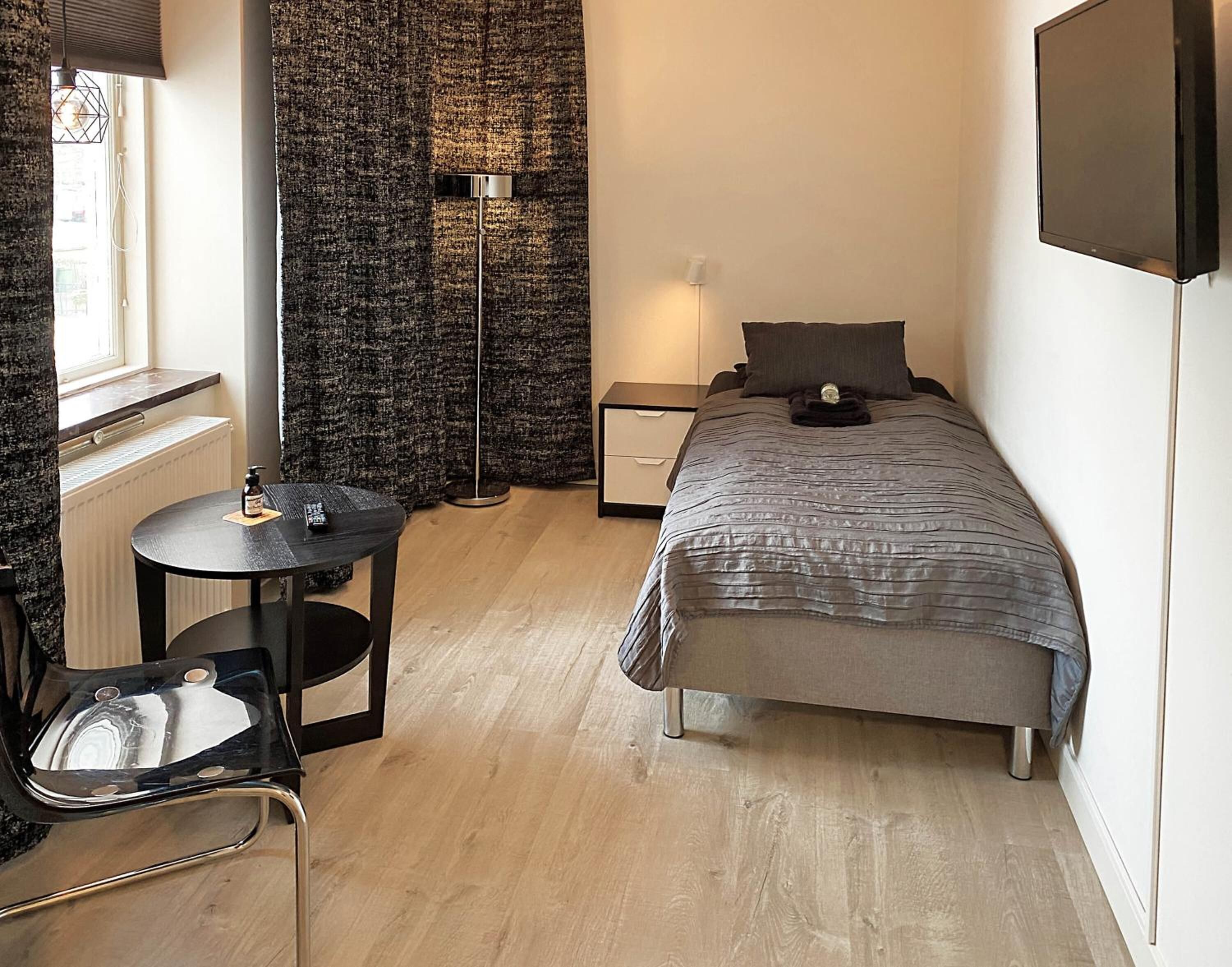 A compact bedroom with a bed, bedside table, chair, and a floor lamp.