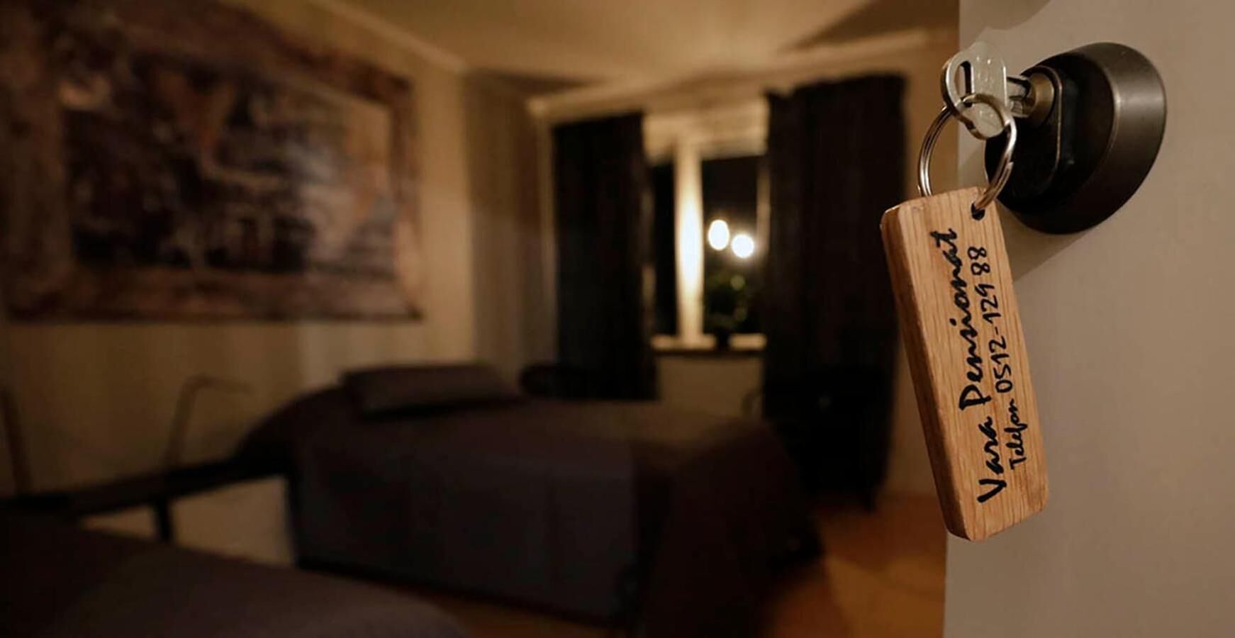 Habitación de hotel con cama, una puerta y tarjeta llave, y un cuadro en la pared.