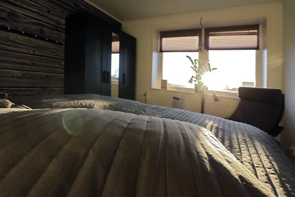 A bedroom with a large bed, a chair, and a window with blinds.