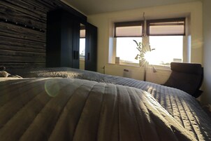 Quarto com uma cama grande, uma cadeira e janela com persianas.