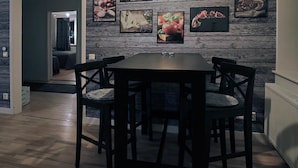 Un comedor con una mesa de madera y cuatro sillas, una pared decorada con cuadros y una puerta visible que da a otra habitación.