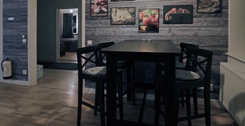 Uma área de refeições com mesa de madeira e quatro cadeiras, parede com quadros e uma porta visível que dá para outro cômodo.