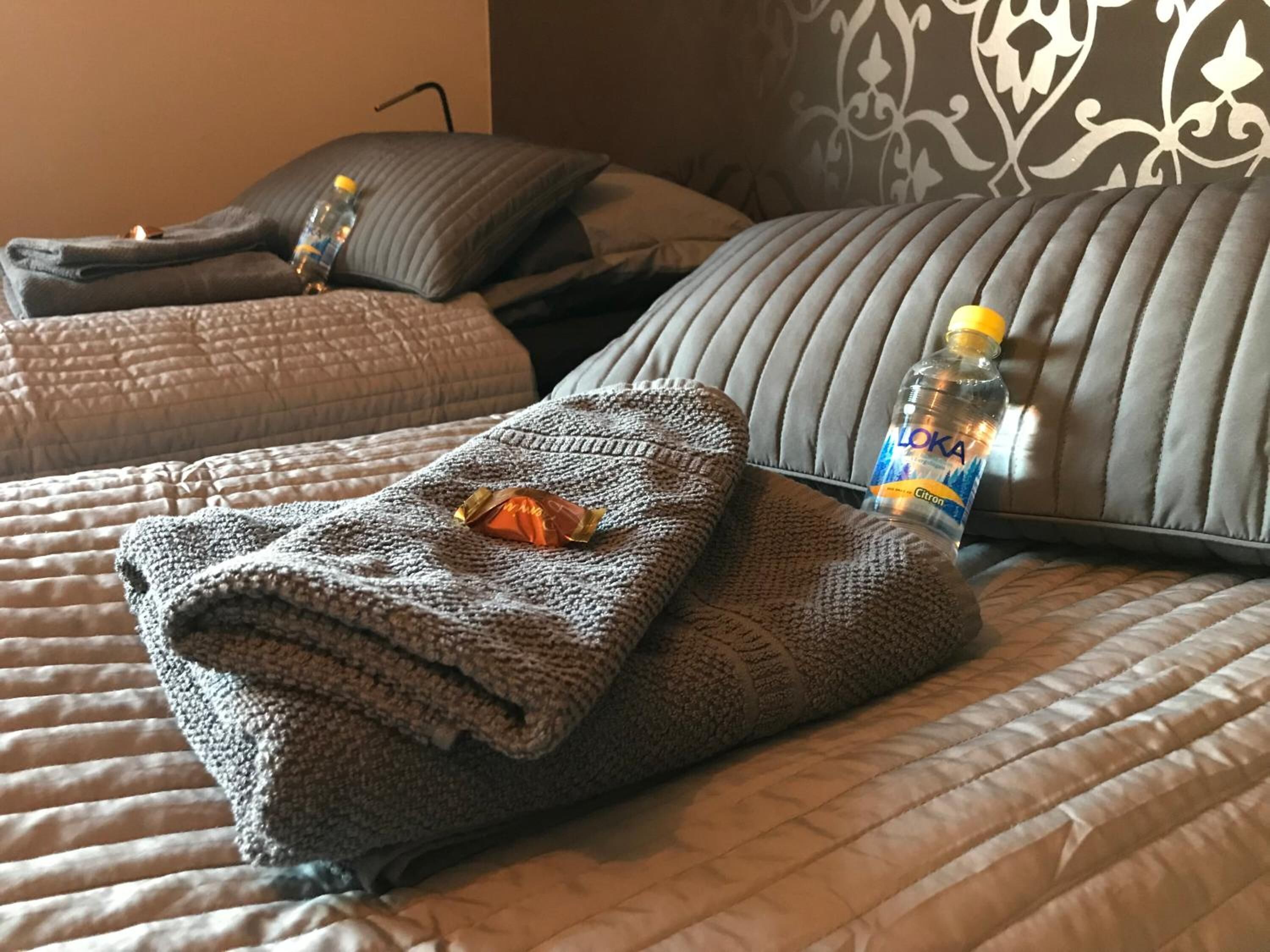 Una cama bien hecha con una manta doblada, una botella de agua y una barra de chocolate.