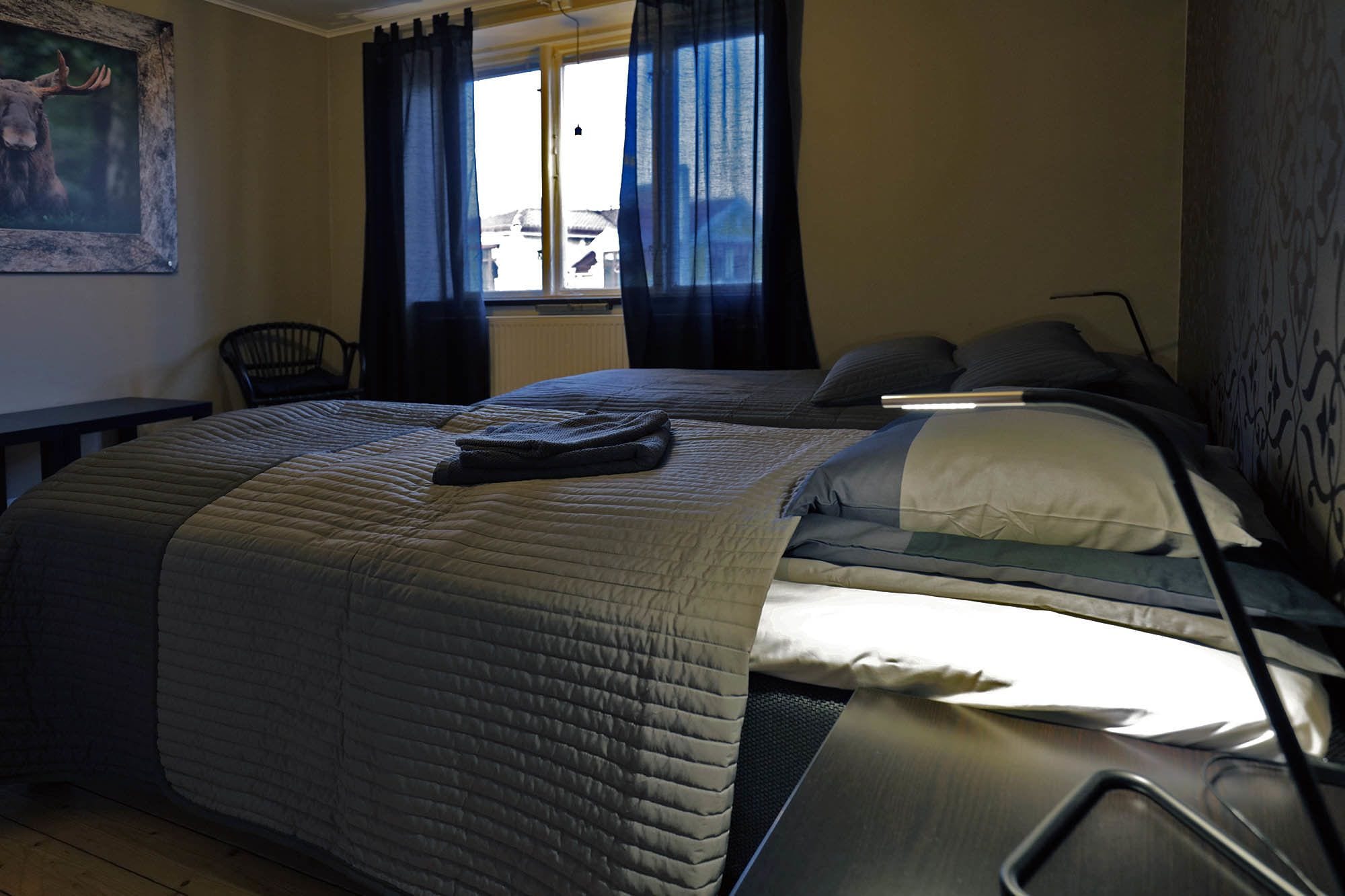 Een hotelkamer met twee bedden, een raam met gordijnen, een stoel en een schilderij aan de muur.