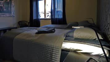 Een hotelkamer met twee bedden, een raam met gordijnen, een stoel en een schilderij aan de muur.