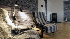 Una habitación acogedora con una pared de madera, una silla negra con una manta de piel, una mesita con una lámpara y una chimenea.