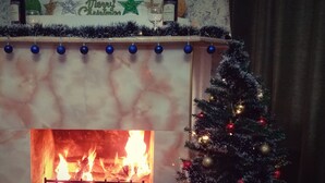 A fireplace with a Christmas tree and decorations, a mantel with bottles and a 'Merry Christmas' sign. - Villa Vera Mini Hotel (Tbilisi)