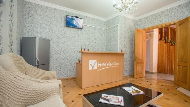 A hotel reception area with a wooden desk, a television, a sofa, and a chandelier. - Villa Vera Mini Hotel (Tbilisi)