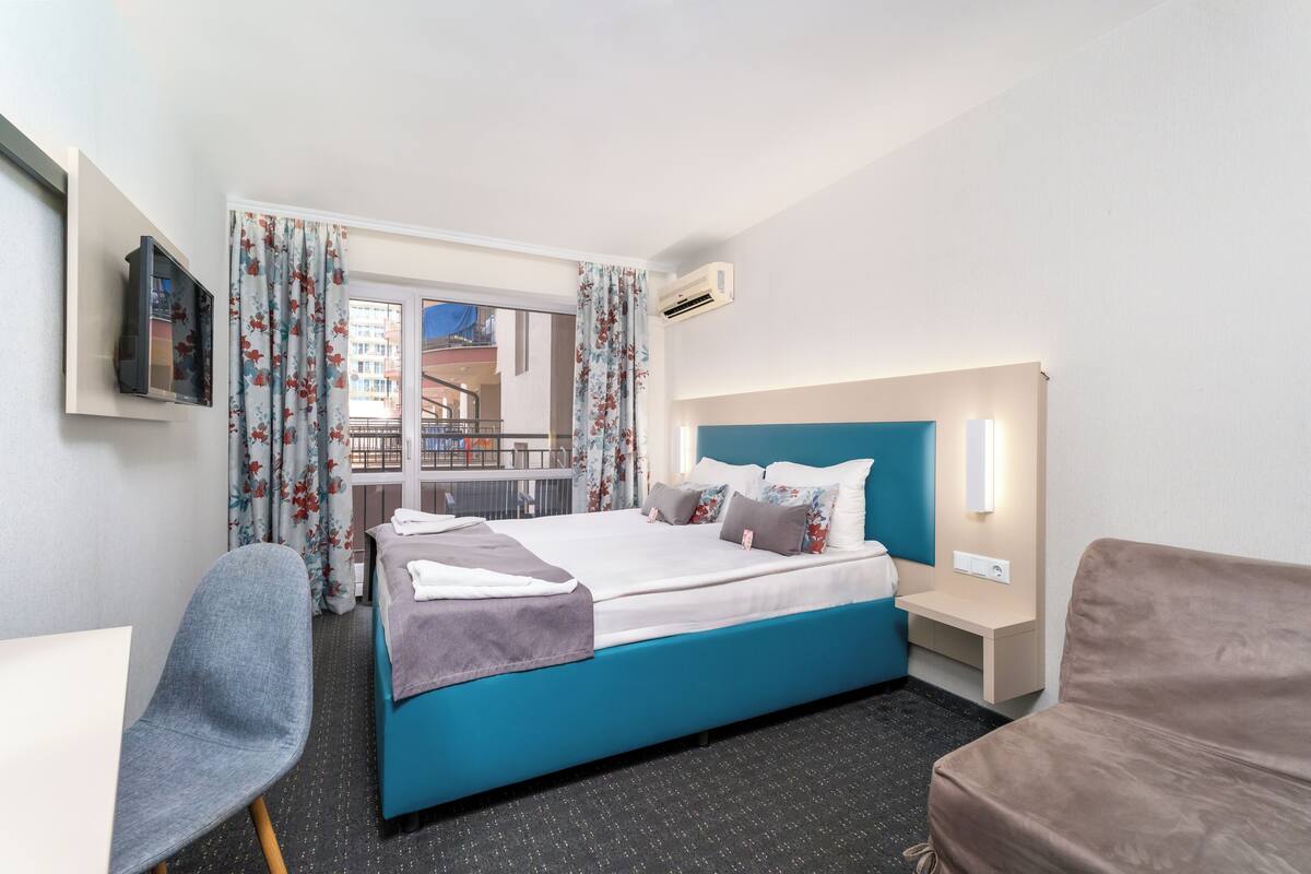 A hotel room with a bed, a chair, a desk, and a TV.