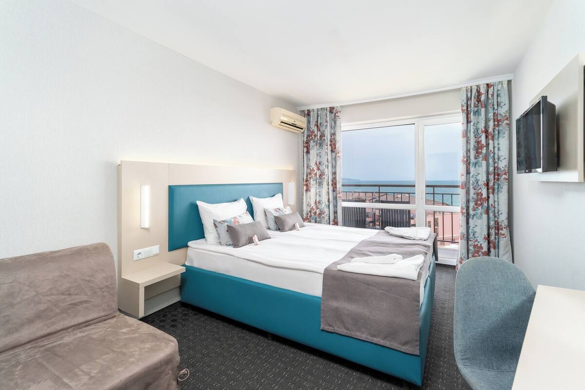 A hotel room with a bed, a sofa, a desk, and a TV.