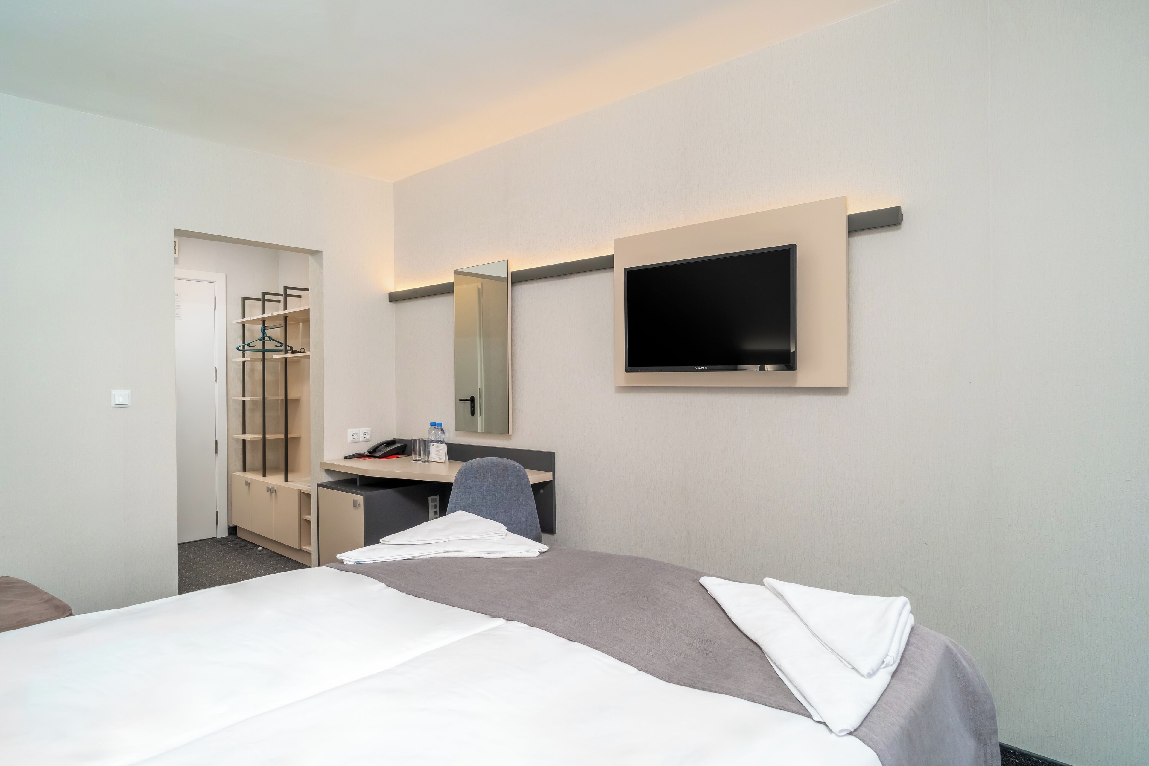 A hotel room with a bed, a desk, a chair, a TV, and a wardrobe.