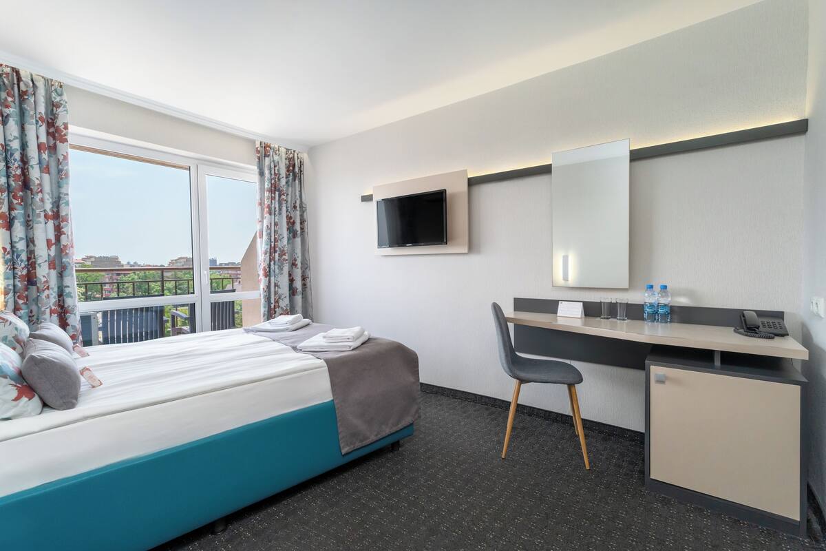 A hotel room with a bed, a desk, a chair, a TV, and a minibar.