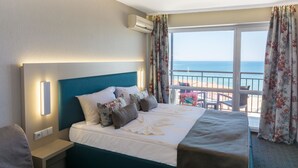 Ein Hotelzimmer mit Bett, Nachttisch, Klimaanlage und Meerblick durch ein großes Fenster.