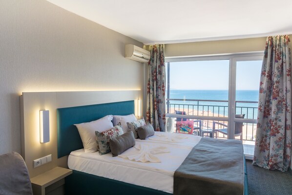 Une chambre d’hôtel équipée d’un lit, d’une table de chevet, d’un appareil de climatisation et offrant une vue sur la mer grâce à une grande fenêtre.