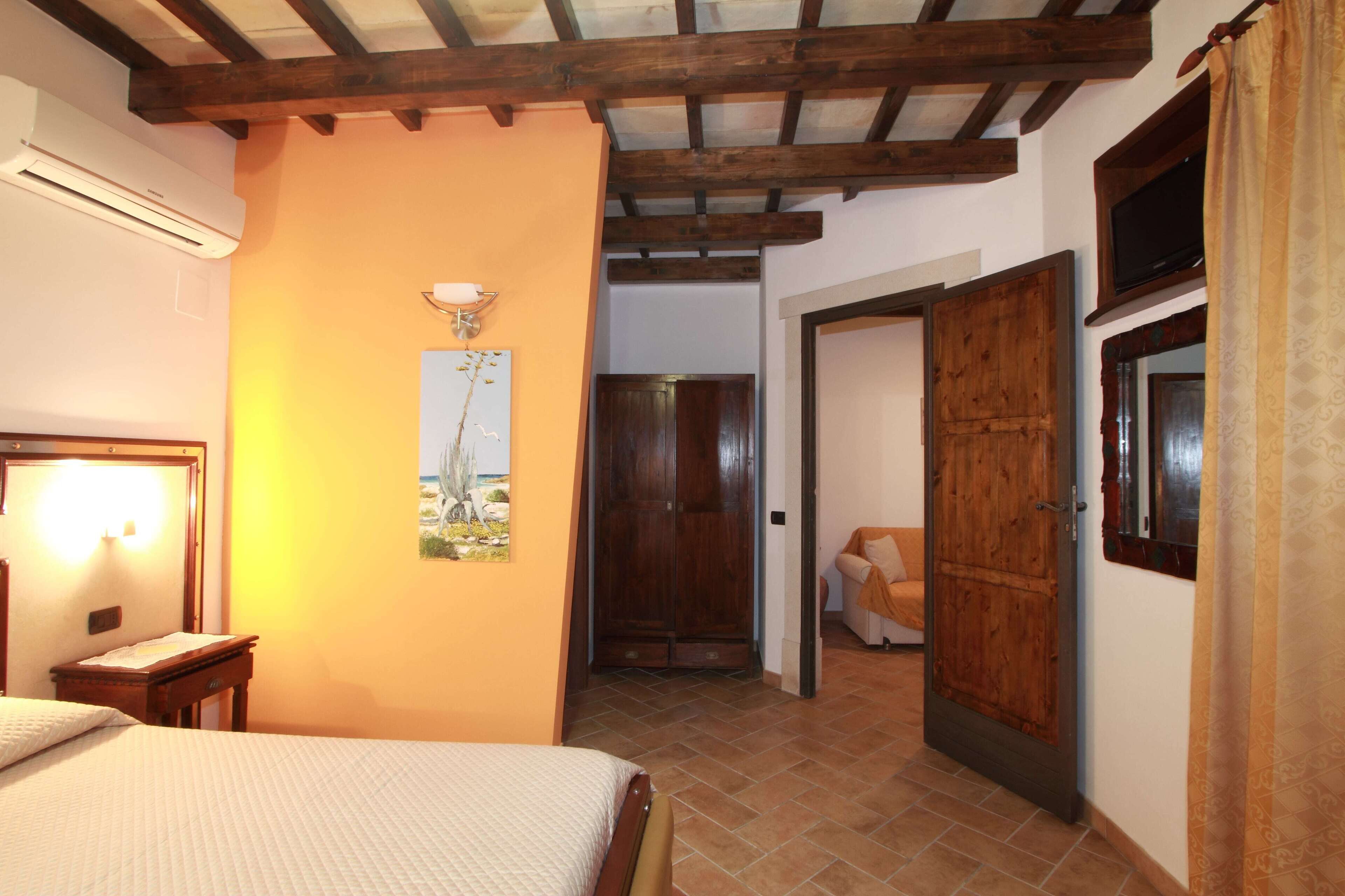 A bedroom with a bed, a nightstand, a wall-mounted lamp, and a door leading to another room.