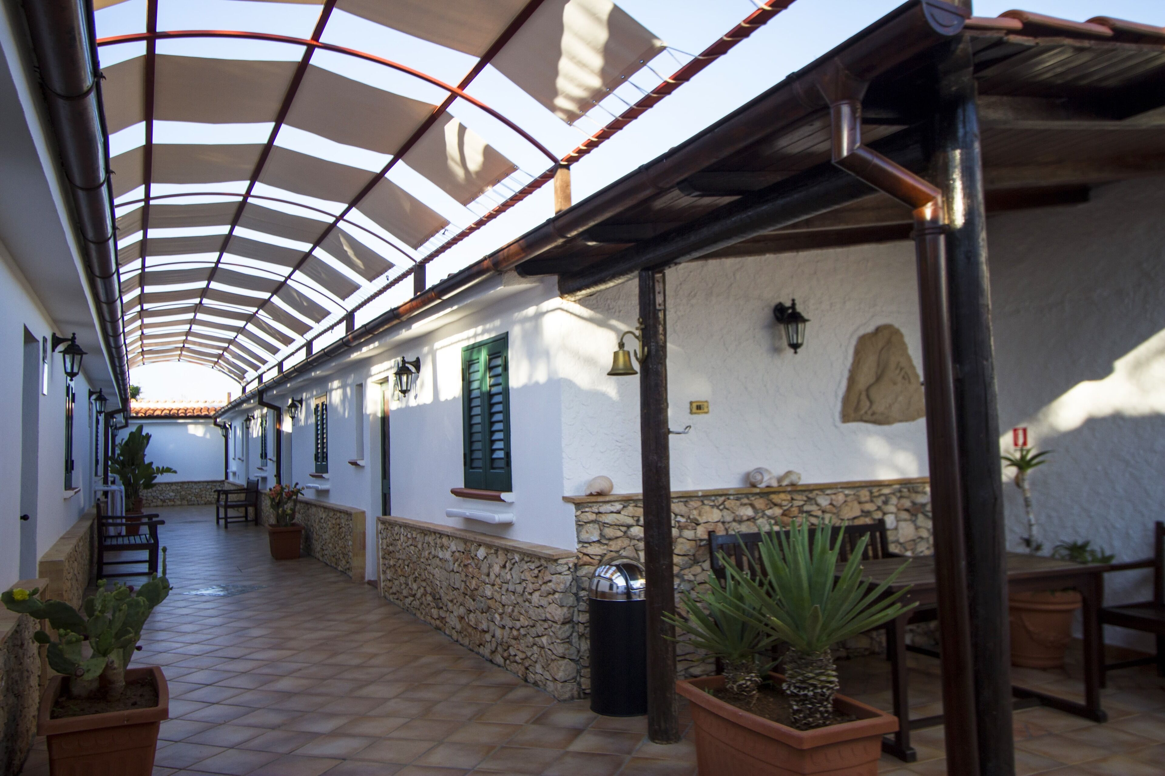 A covered outdoor corridor with stone walls, potted plants, and outdoor furniture.