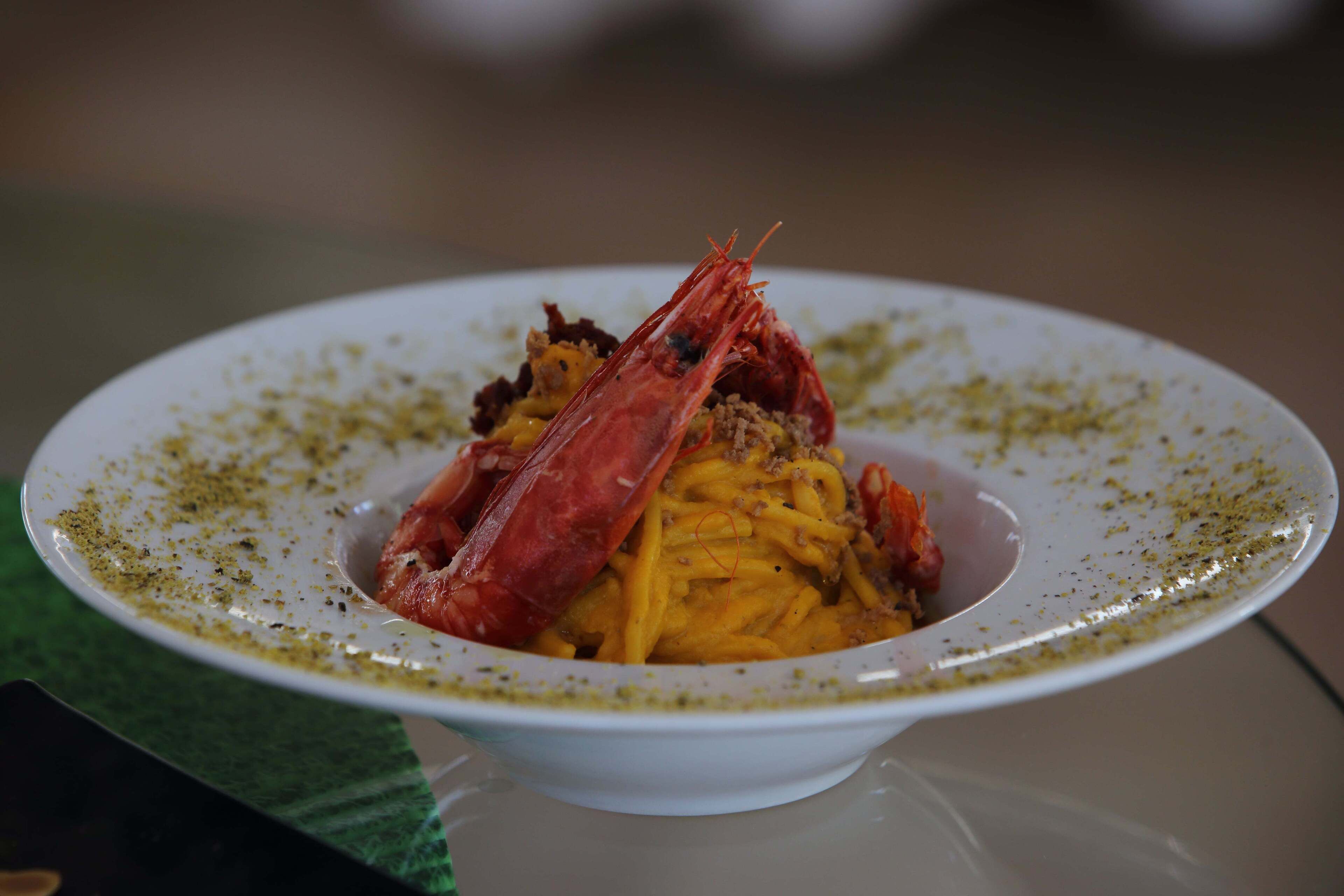Lautasella on spagettia, jonka päällä on suuri katkarapu ja annos on koristeltu yrteillä.