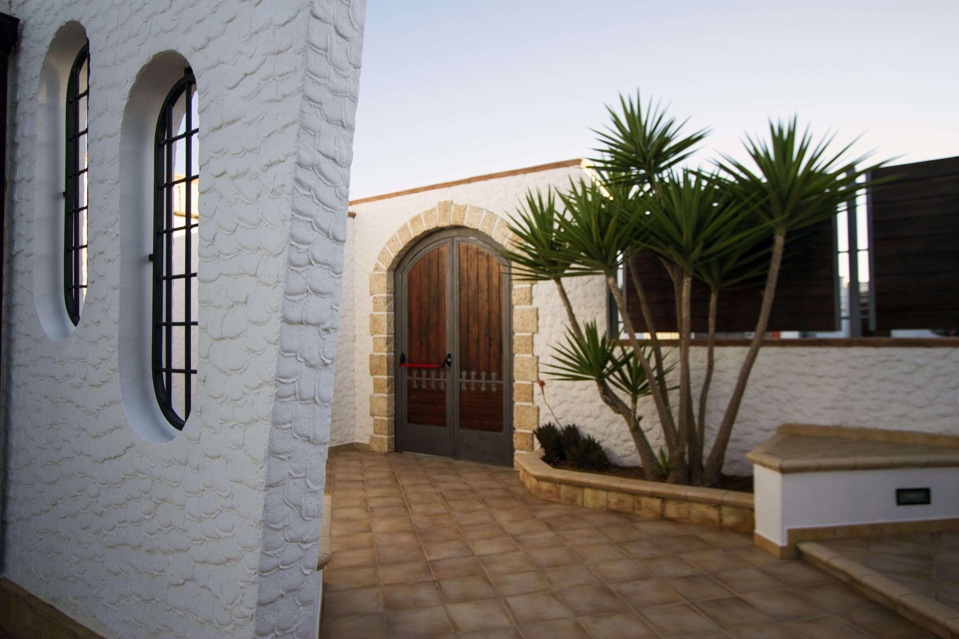 A building with a white exterior, a wooden door, and a tiled entrance area.
