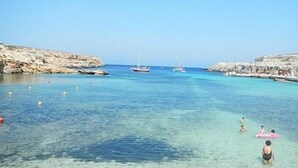 Uma área costeira com águas cristalinas, terreno rochoso e barcos.