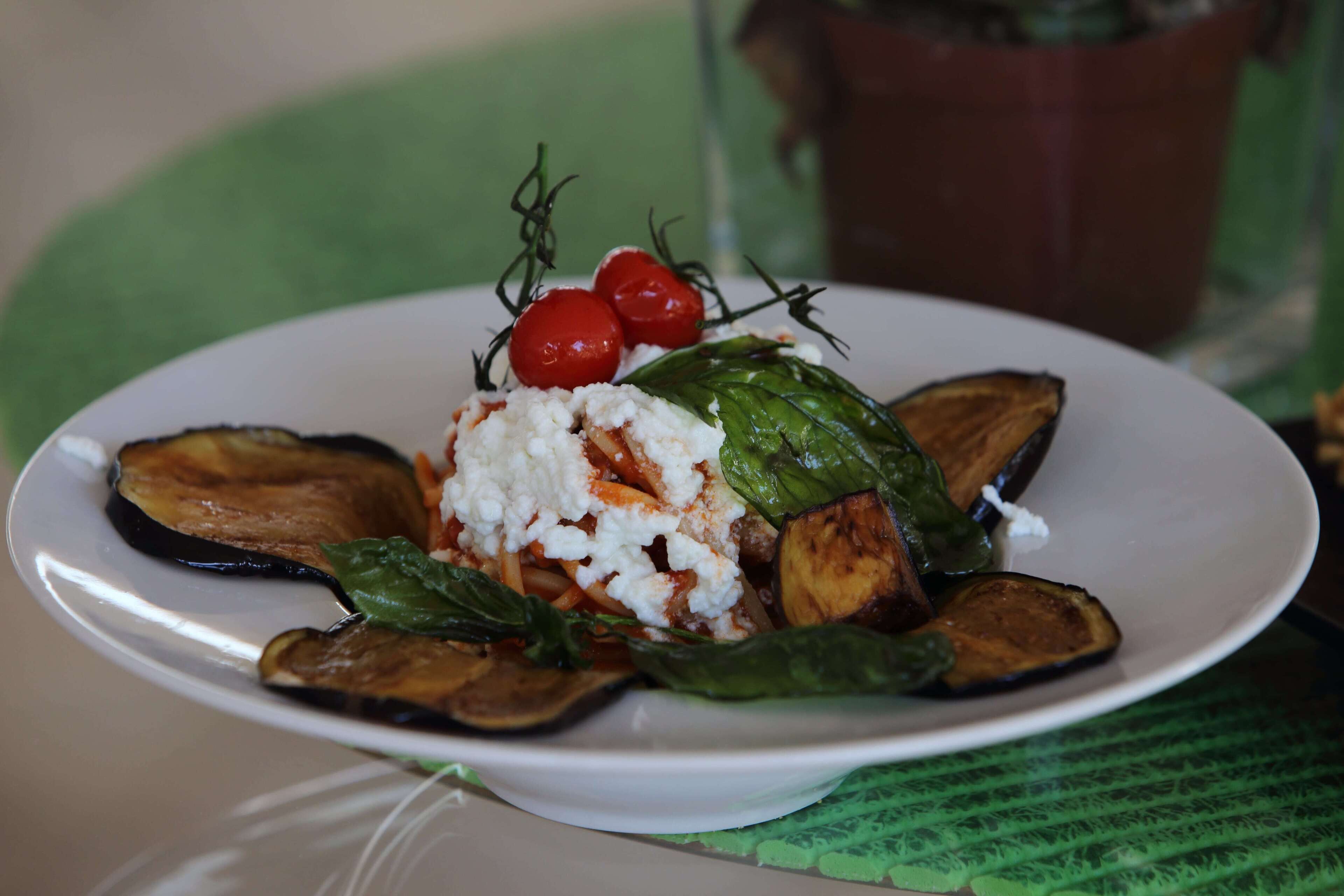 A plate of food with roasted vegetables and a dollop of white sauce, garnished with cherry tomatoes and herbs, on a white plate.