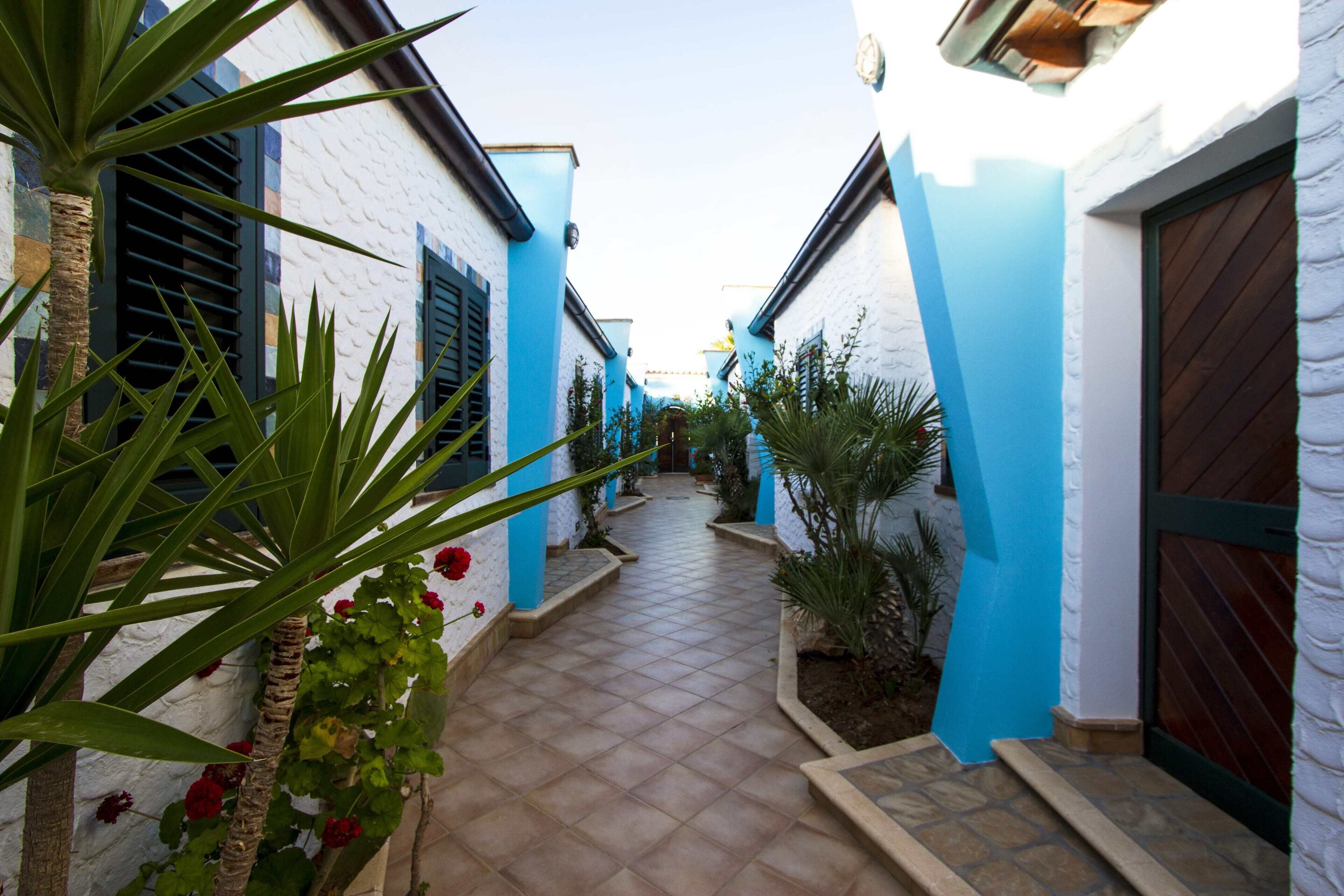 A narrow pathway flanked by buildings with blue and white walls, leading to a door.