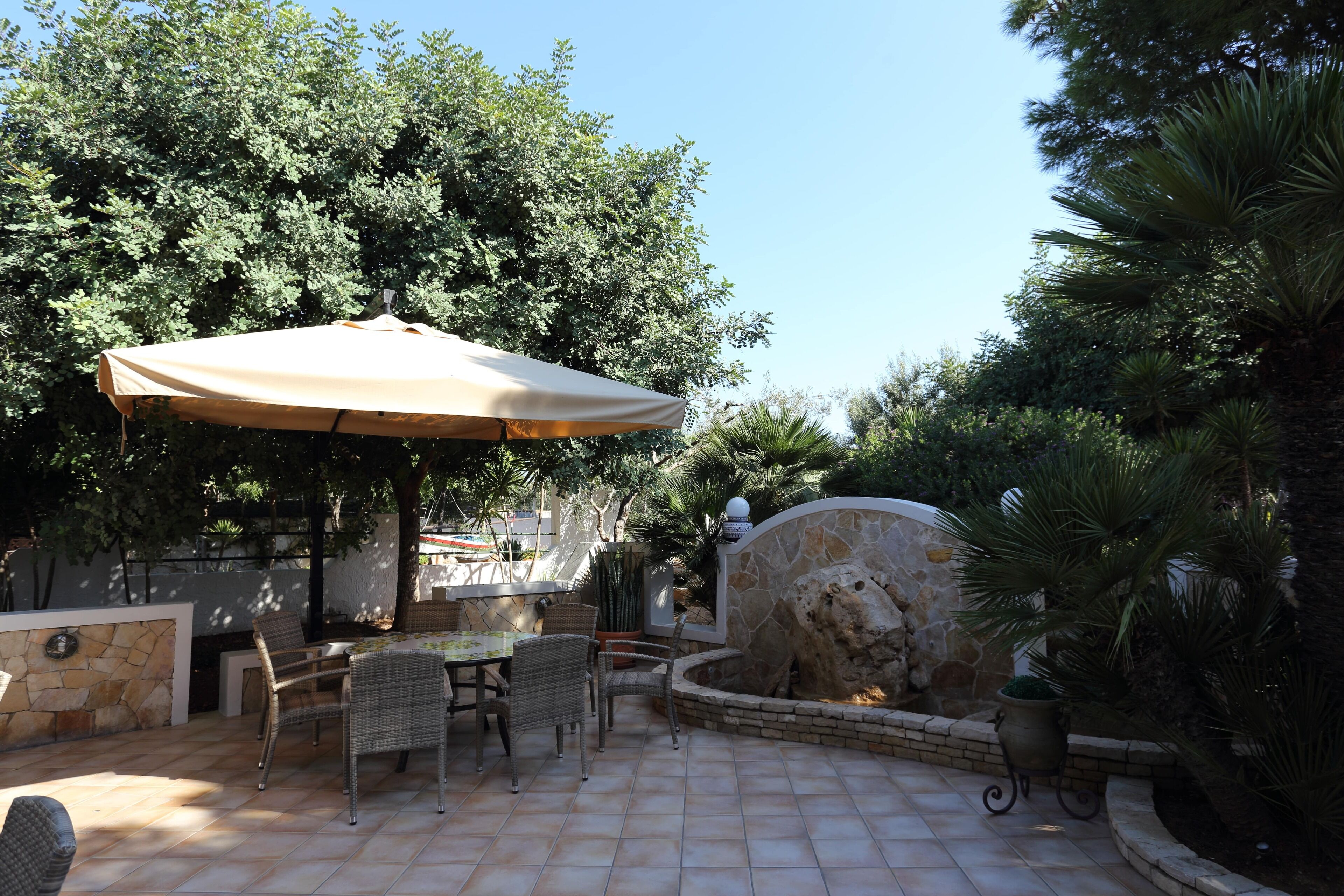 Une terrasse extérieure avec une table et des chaises, entourée de murs en pierre et de verdure.