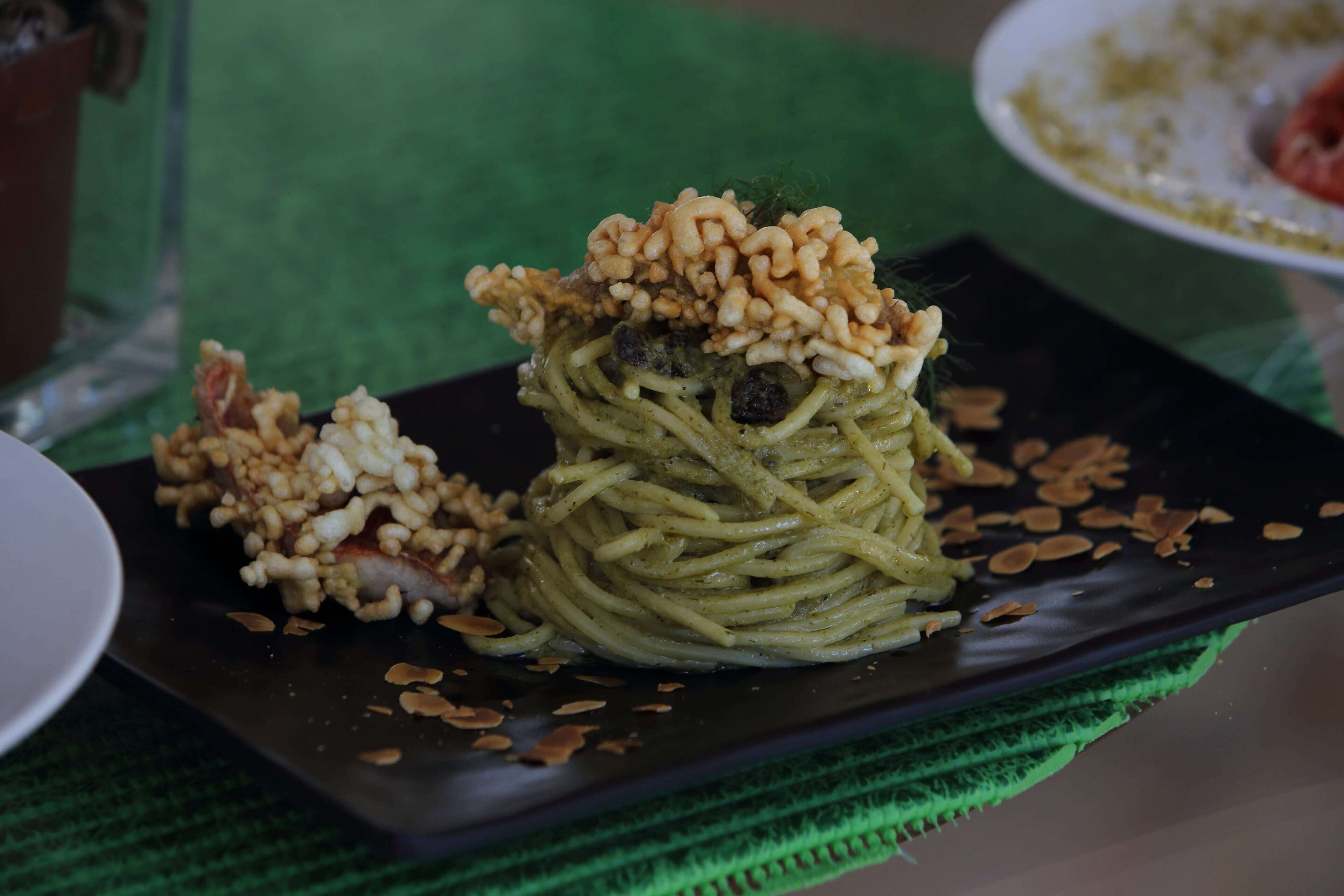 A plate of pasta with a topping of nuts and a small portion of sauce on a dark plate.