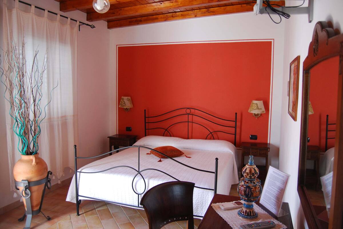 Una camera da letto con un letto, una sedia, un tavolo con un vaso e uno specchio.