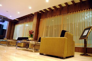 Vestíbulo de hotel con mostrador de recepción, zona de estar y ventanas grandes con cortinas.