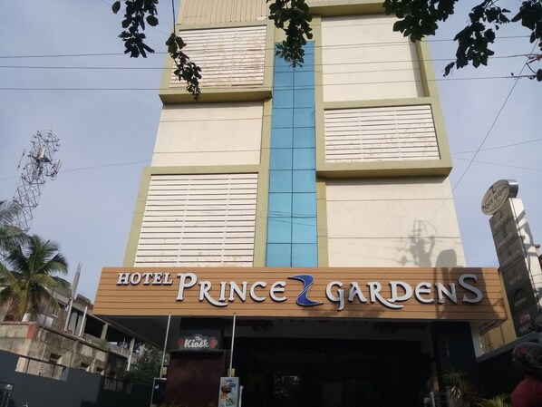 Exterior del Hotel Prince Gardens, con un letrero destacado con el nombre del hotel, una franja vertical azul y un cartel de quiosco debajo.