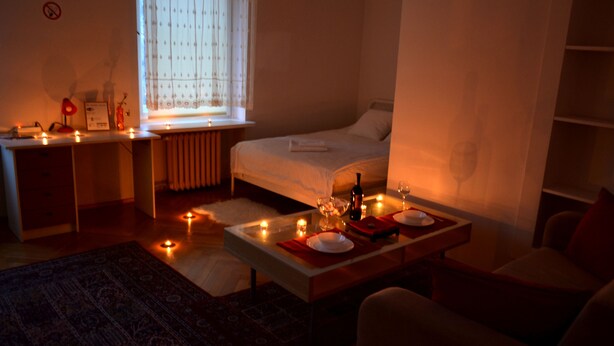A dimly lit room with a bed, a desk, and a dining table set for two. - West Apartments Mazowiecka 7 (Warsaw)