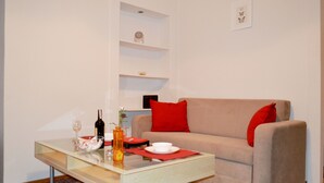 A modern living room with a glass coffee table, a beige sofa with red cushions, a red rug, and a minimalist shelving unit against the wall. - West Apartments Mazowiecka 7 (Warsaw)