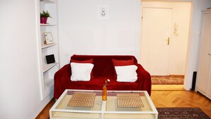 A living room with a red sofa, white cushions, a small table with a vase, and a bookshelf. - West Apartments Mazowiecka 7 (Warsaw)