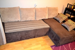 Un sofá cama con cojines estampados, suelo de madera y una silla.