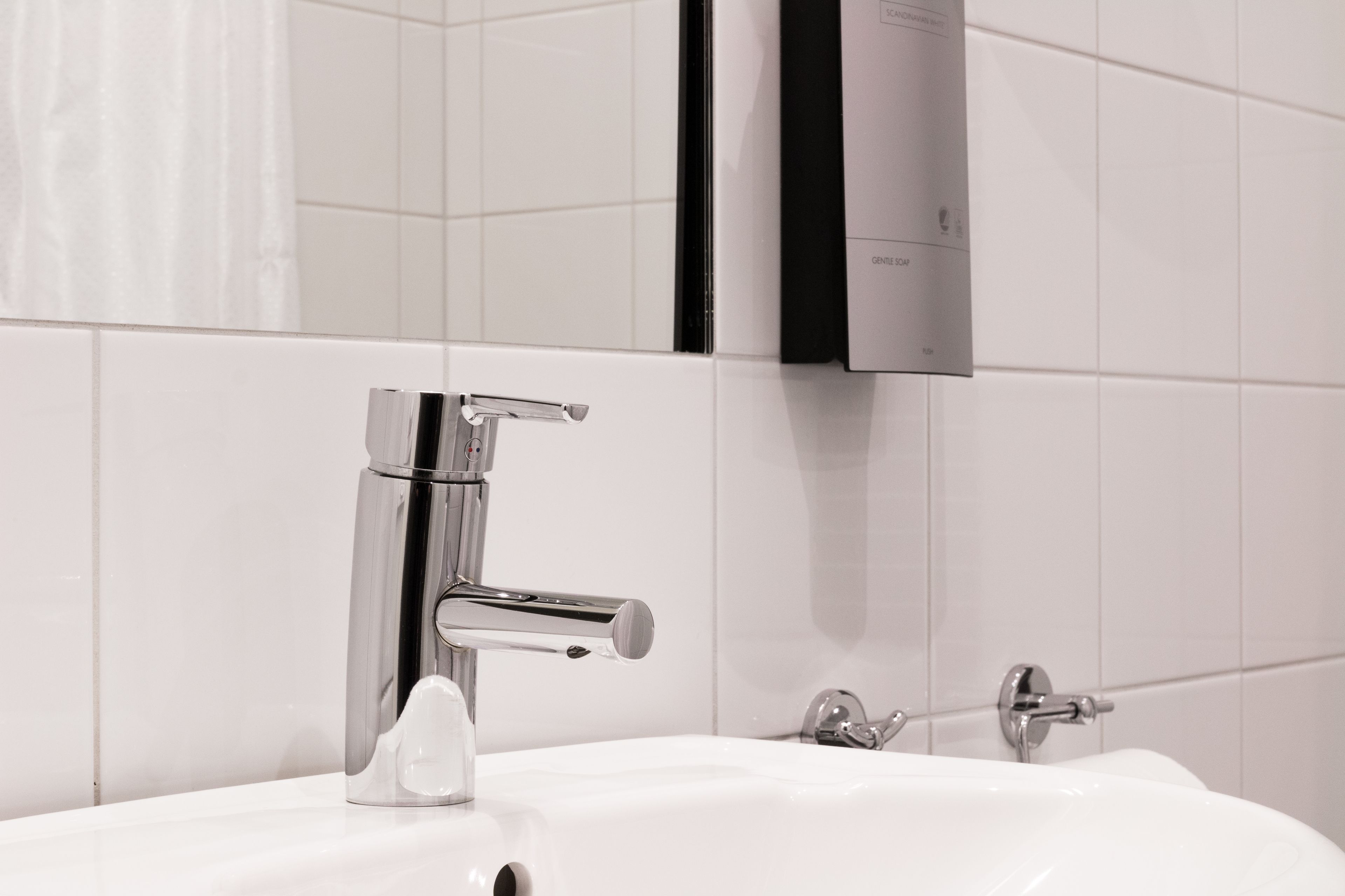 A modern bathroom with a chrome faucet, a white sink, and a towel rack.