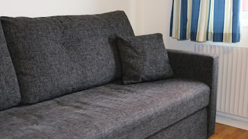 Un sofá gris con un cojín a juego en una habitación con radiador y cortinas a rayas.