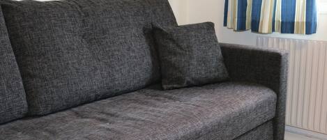 A grey sofa with a matching pillow in a room with a radiator and striped curtains.
