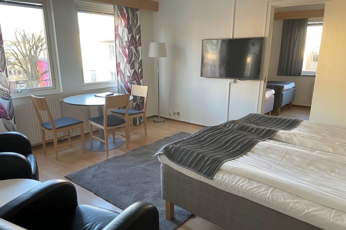 Habitación de hotel con cama, escritorio, dos sillas, televisor y ventana con cortinas.
