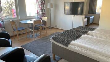 Habitación de hotel con cama, escritorio, dos sillas, televisor y ventana con cortinas.