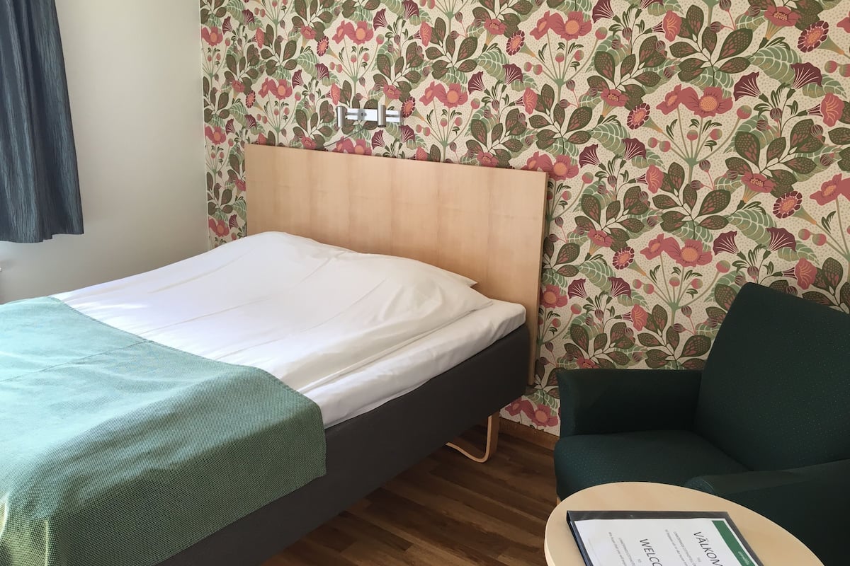 Una habitación de hotel con una cama, un sofá verde, un cabecero de madera y un papel tapiz floral.
