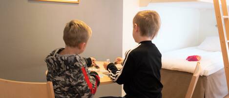 Zwei Kinder spielen Karten an einem Tisch in einem Zimmer mit einem Etagenbett und einem gerahmten Bild an der Wand.
