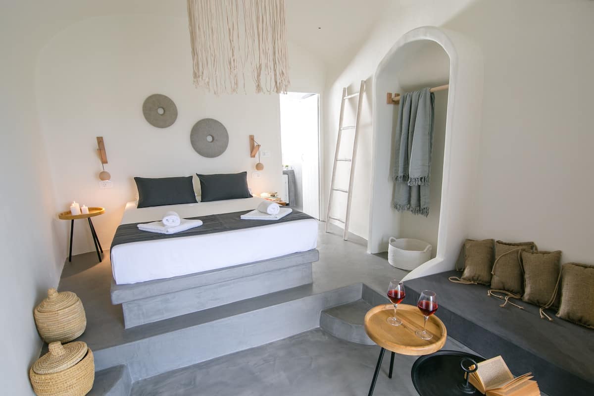 A modern bedroom with a large bed, a small table with wine glasses, and a cozy seating area.