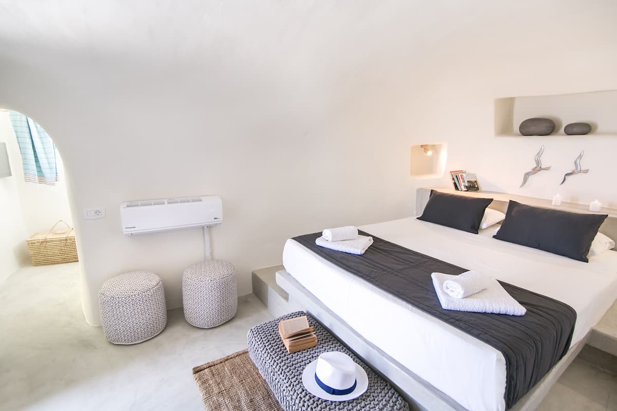 A modern bedroom with a large bed, bedside tables, a wall-mounted air conditioner, and a basket on the floor.