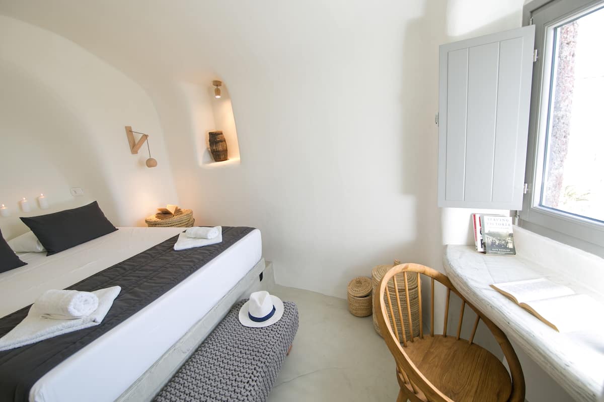 A bedroom with a bed, bedside table, chair, and a window with books.