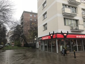 Un restaurant servant des steaks, reconnaissable à son enseigne rouge et blanche, situé au coin d’une rue dont le trottoir est pavé de briques.